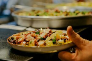 A vibrant dish of octopus and potatoes garnished with herbs, presented on a ceramic plate.